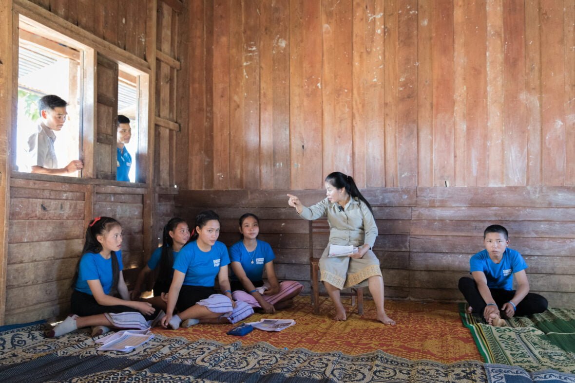 Opettaja ja viisi nuorta koululuokassa keskustelemassa Laosissa.