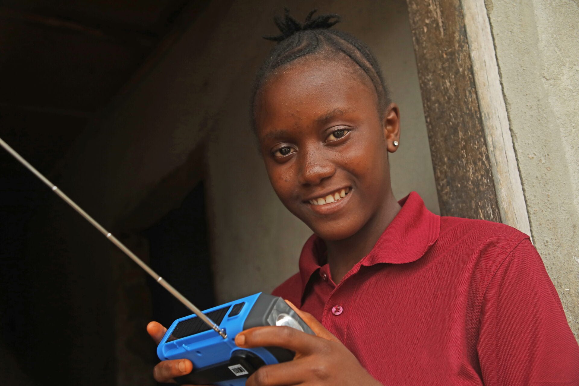 Sierraleonelainen tyttö pitelee sinistä radiota kädessään ja hymyilee.