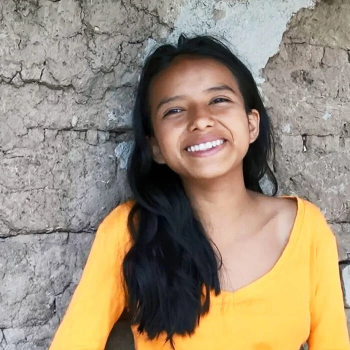 Ecuadorilainen tyttö nojaa hymyillen kiviseen seinään.