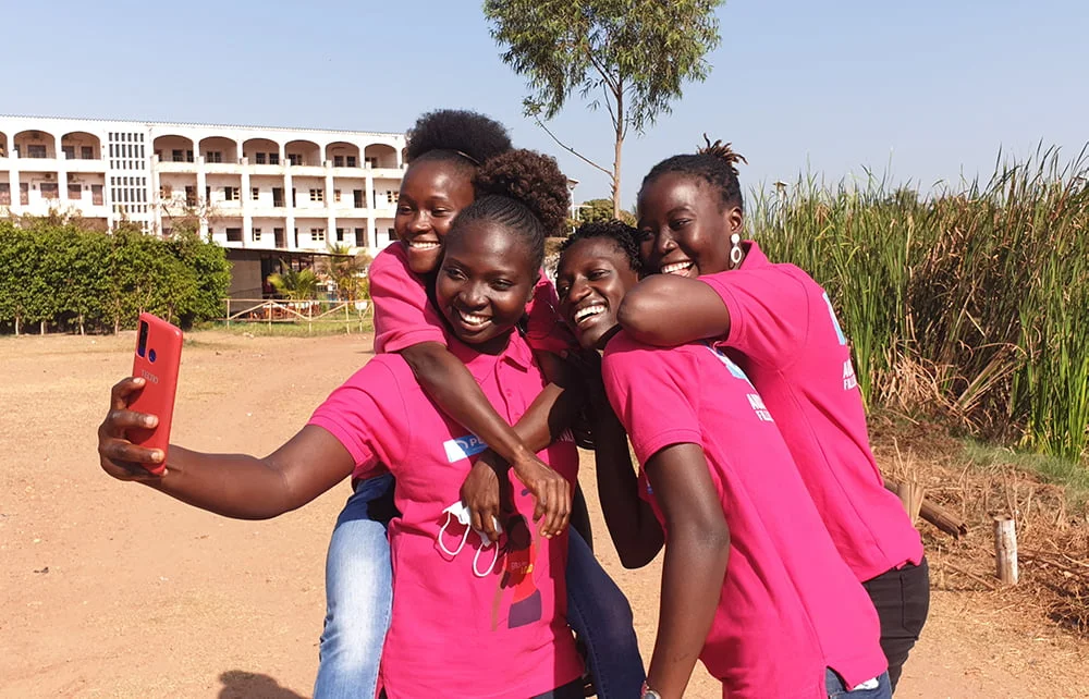 Neljä pinkkeihin paitoihin pukeutunutta nuorta ottaa nauraen selfietä Guinea-Bissaussa.