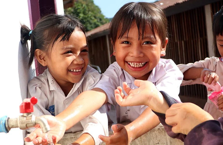 Nauravia tyttöjä pesemässä yhdessä käsiään Laosissa.