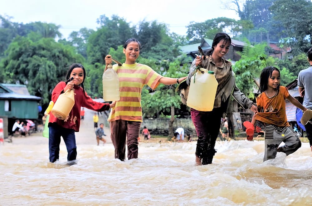 Kaksi naista ja kaksi tyttöä kävelevät vesikanistereiden kanssa tulvivassa vedessä.
