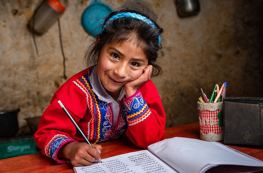 Perulainen tyttö istuu pöydän ääressä tekemässä koulutehtäviä.