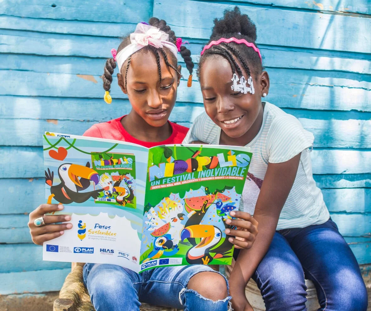 Kaksi kolumbialaista tyttöä lukee lasten lehteä ja hymyilee.