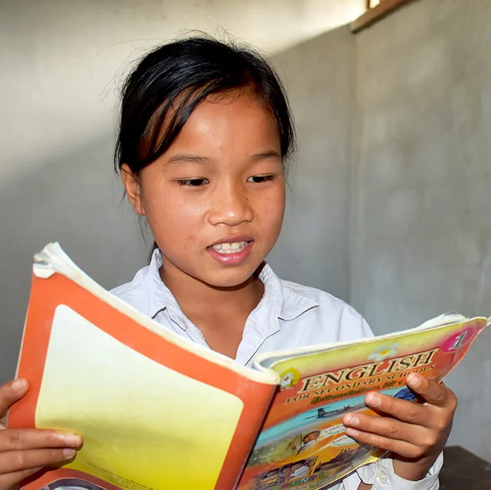 Laosilainen tyttö lukee oppikirjaa koululuokassa.