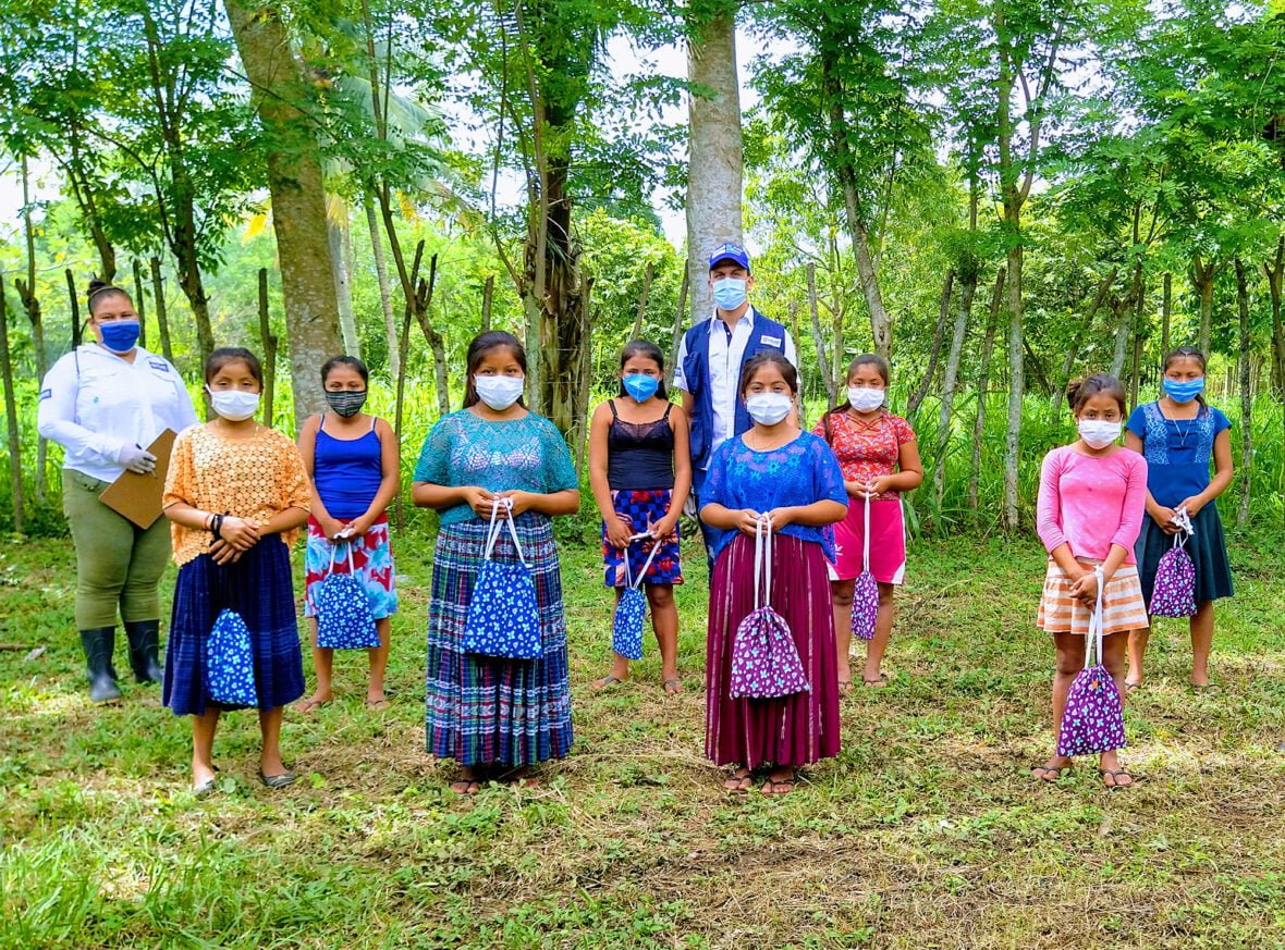 Planin työntekijöitä ja naisia maskit päällä metsän reunassa Guatemalassa.