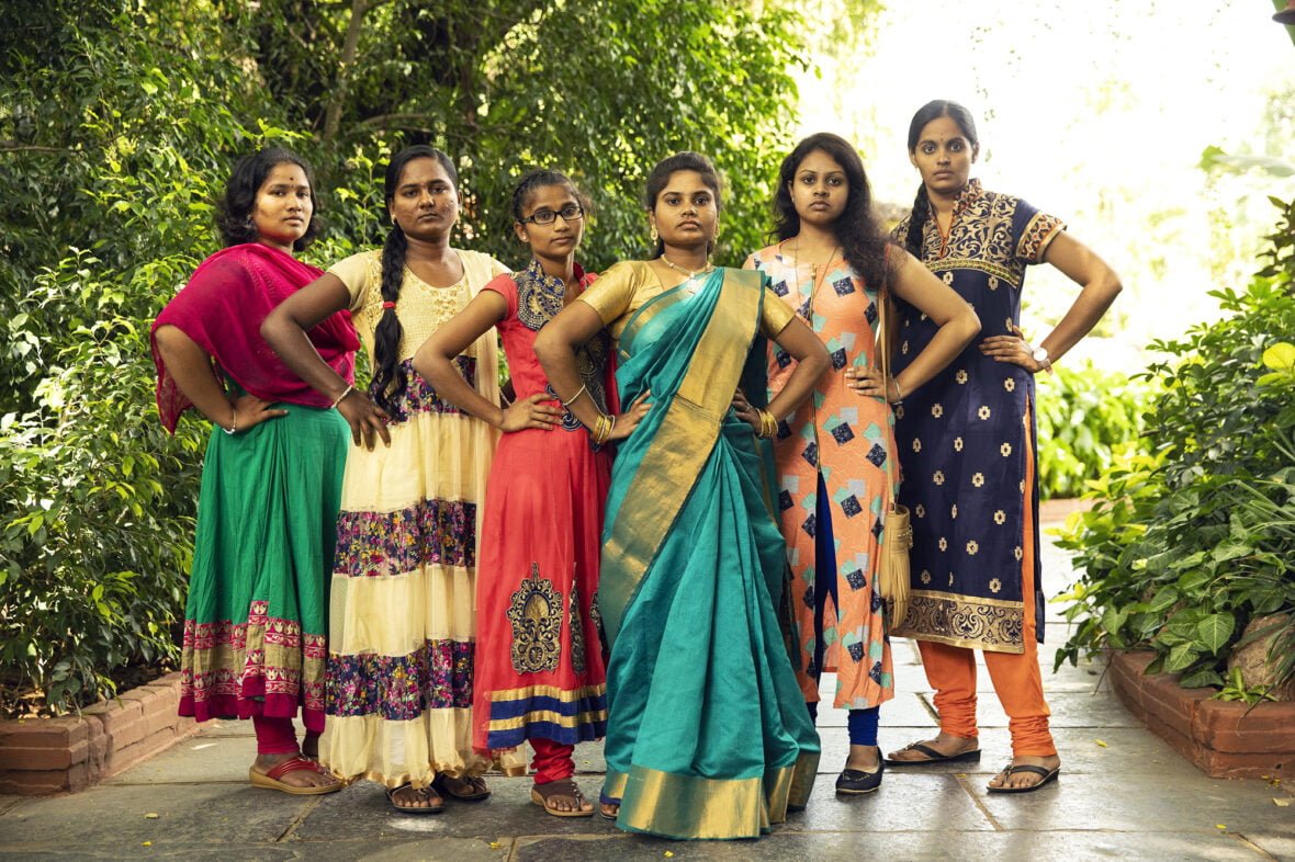 Kuusi intialaista tyttöä poseeraa vakavana kädet lanteilla.