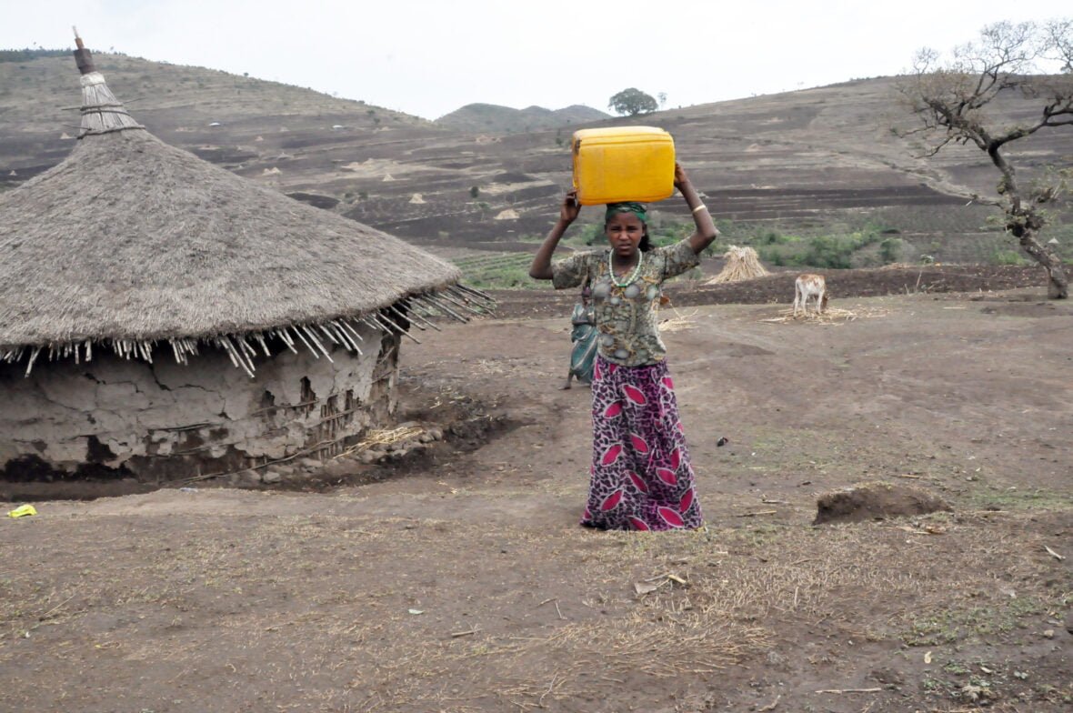 Etiopialainen tyttö kantaa keltaista vesikanisteria kuivassa maastossa.