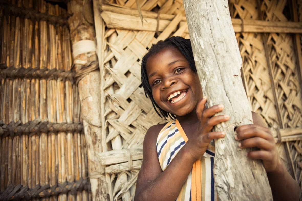 Mosambikilainen tyttö nojaa pylvääseen ja hymyilee.