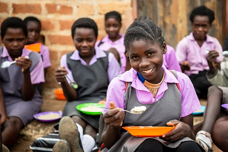 Sambialaiset tytöt ruokailevat pihalla.
