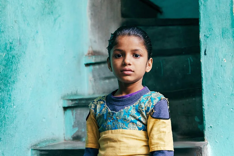 Intialainen tyttö seisoo portaikon edessä ja katsoo kameraan.