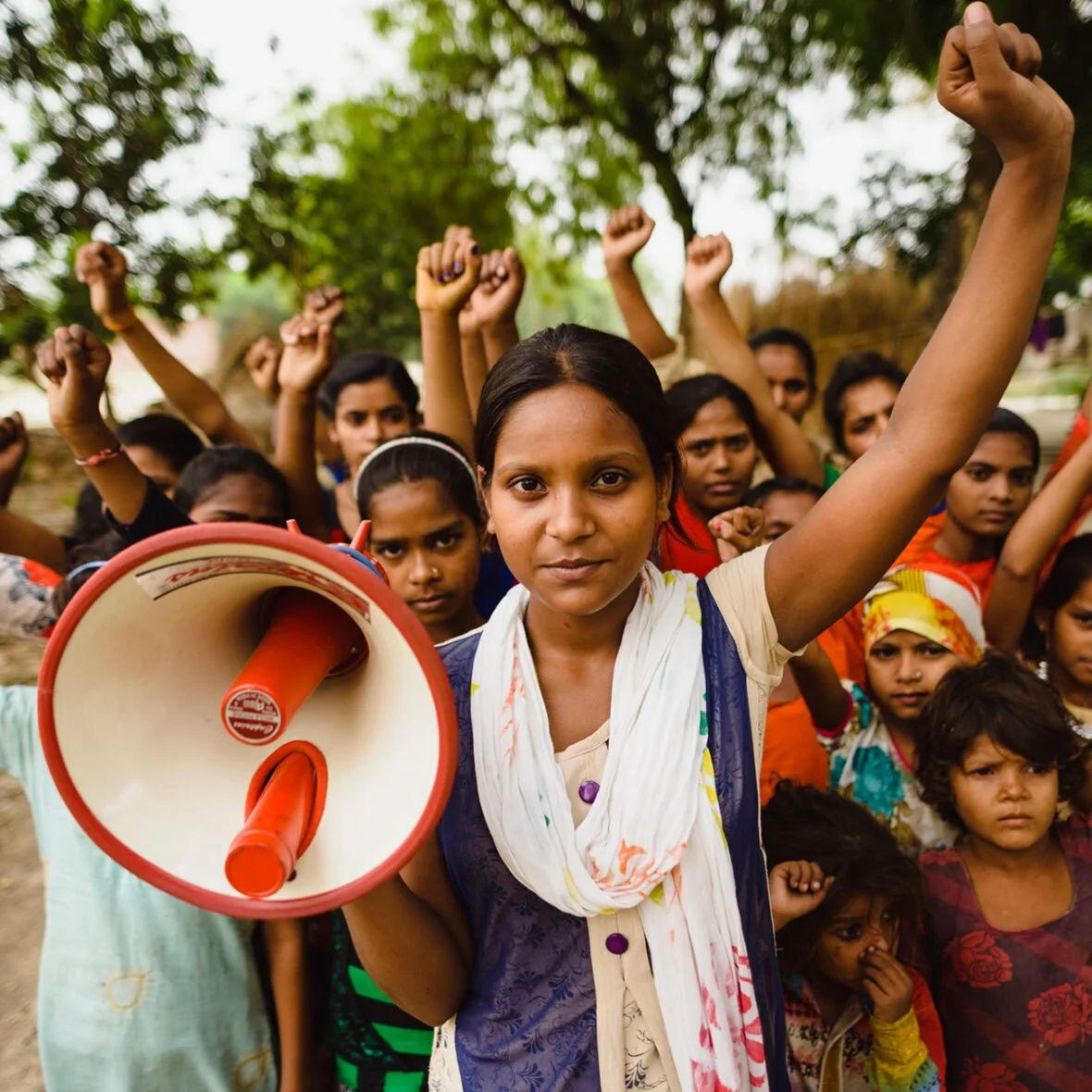 Joukko intialaisia tyttöjä on nostanut kätensä ilmaan. Yhdellä tytöistä on megafoni kädessään.