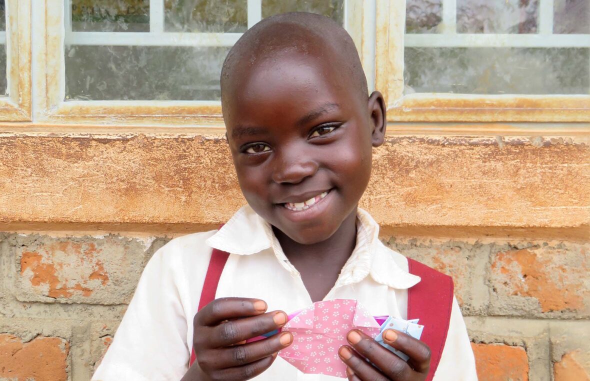 Ugandalainen tyttö pitelee kädessään vaaleanpunaista origamia.