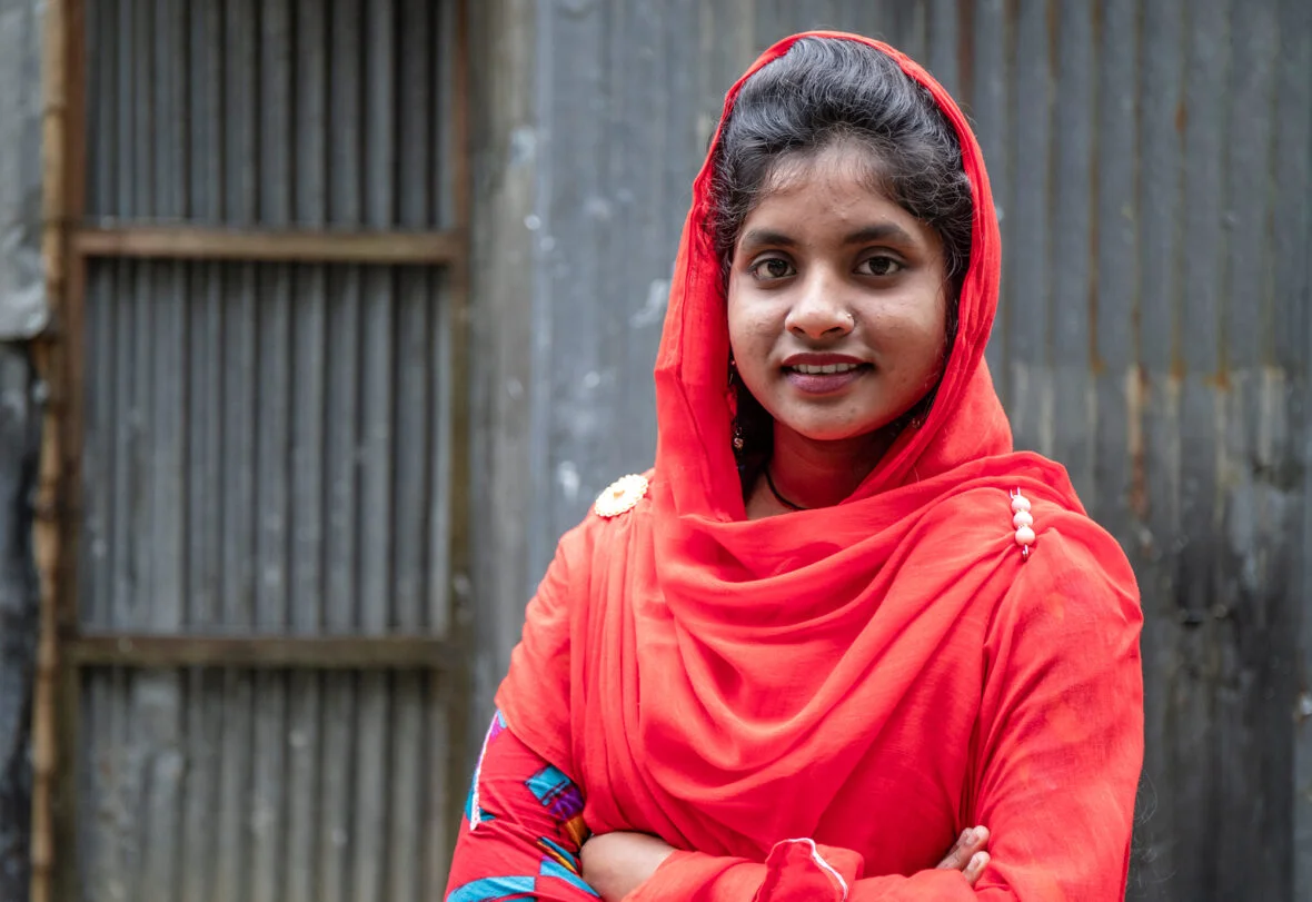 Bangladeshilainen tyttö seisoo kädet puuskassa ja katsoo kohti kameraa.