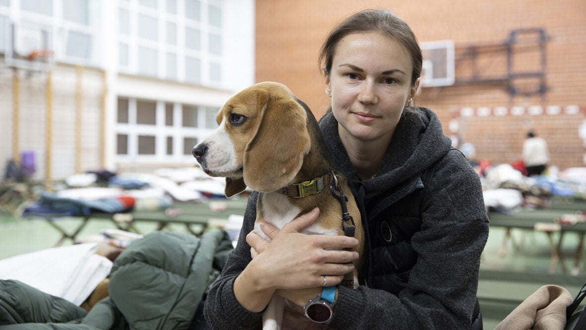 Ukrainalainen Yana, 33, istuu väliaikaisessa vastaanottokeskuksessa urheiluhallissa koira sylissään.
