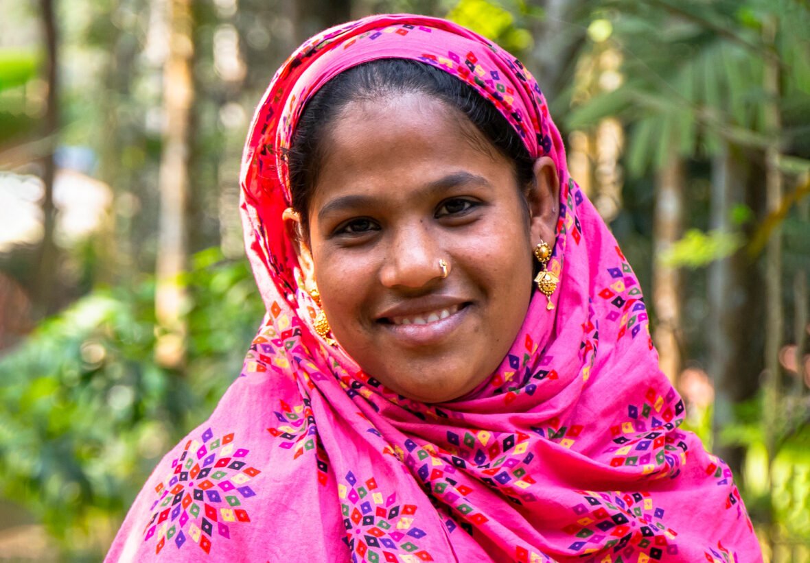 Bangladeshilainen nuori nainen katsoo hymyillen kameraan.