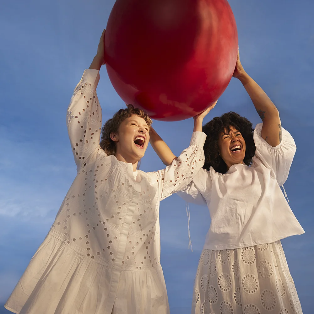 Kaksi tyttöä kannattelee kasissaan suurta punaista palloa, tyttösponssina nujerrat kuukautissyrjintää ja puolustat tasa-arvoa