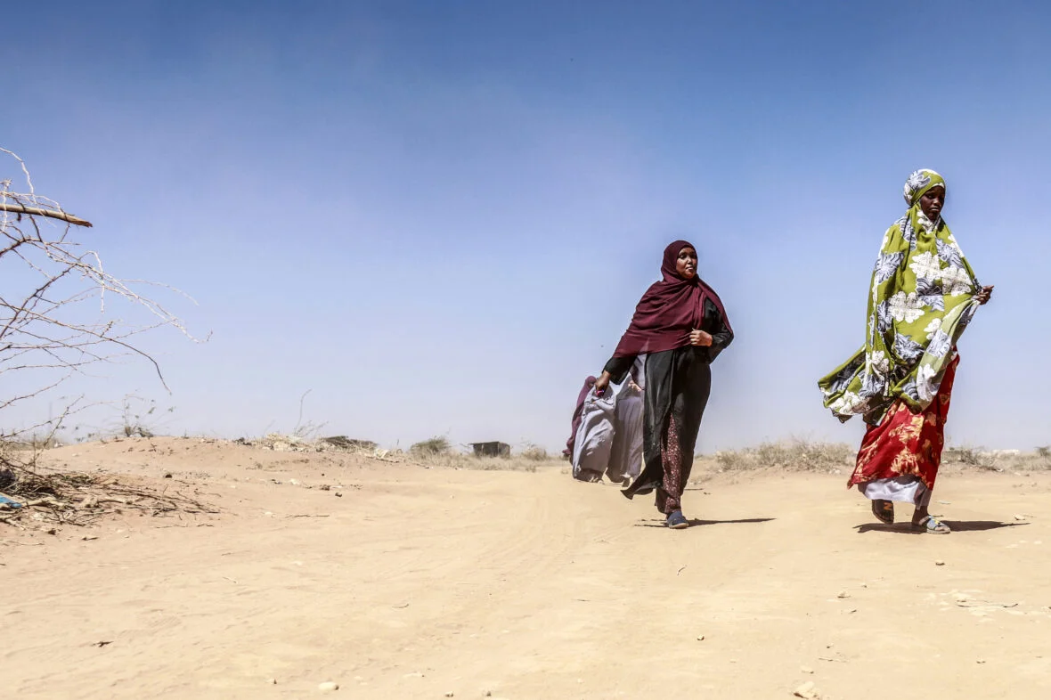 Joukko naisia kävelee kuivalla hiekka-aavikolla auringonpaahteessa Somaliassa.