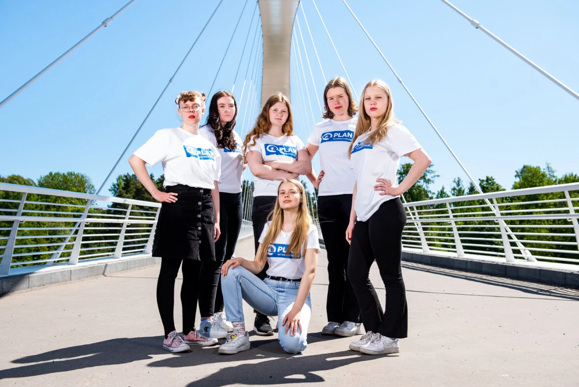 Kuusi Planin #GirlsTakeover-nuorta poseeraa sillalla aurinkoisessa säässä.