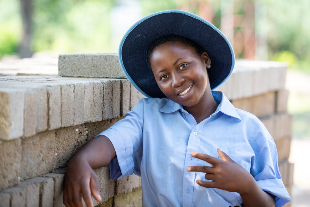 Zimbabwelainen tyttö hymyilee tiilimuurin edessä.