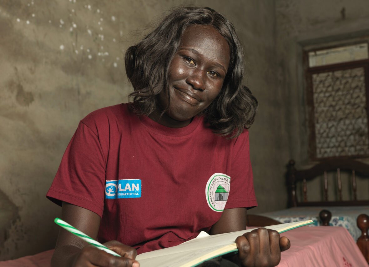 Eteläsudanilainen nuori aktivisti istuu sängyn reunalla kirja kädessään.
