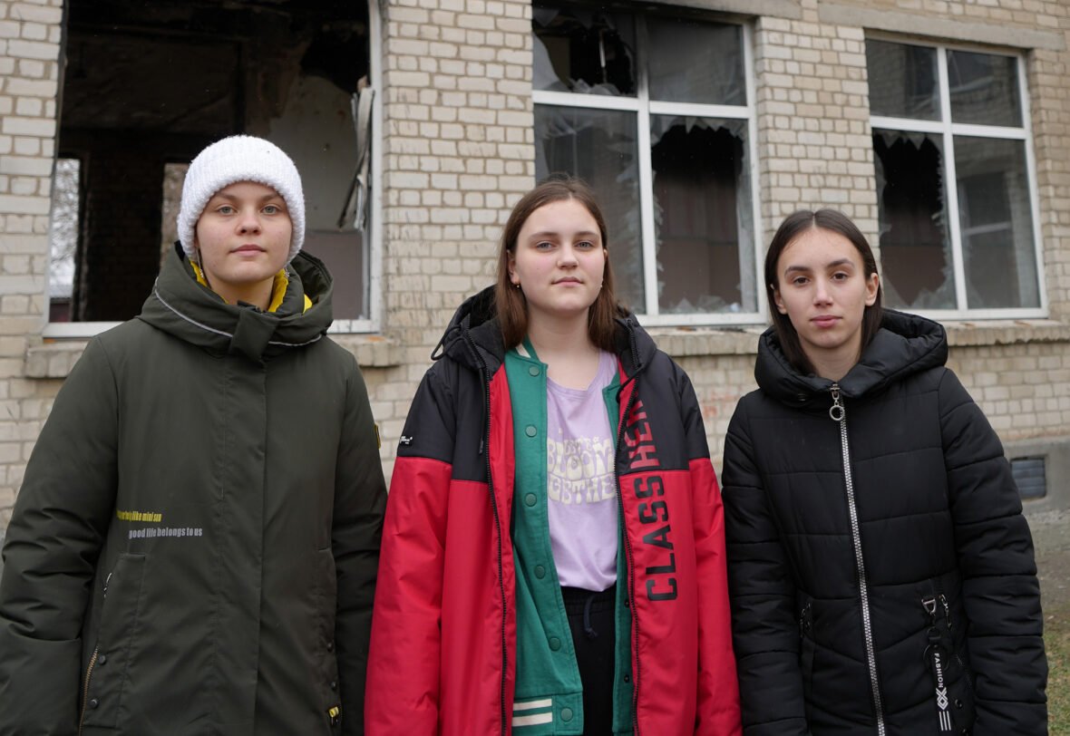 Kolme ukrainalaista tyttöä seisoo vaurioituneen koulun edessä.