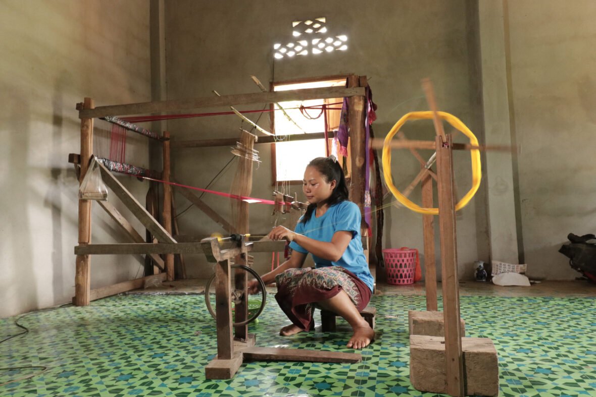 Laosilainen Sipheng valmistelee lankarullia isojen kangaspuiden äärellä.