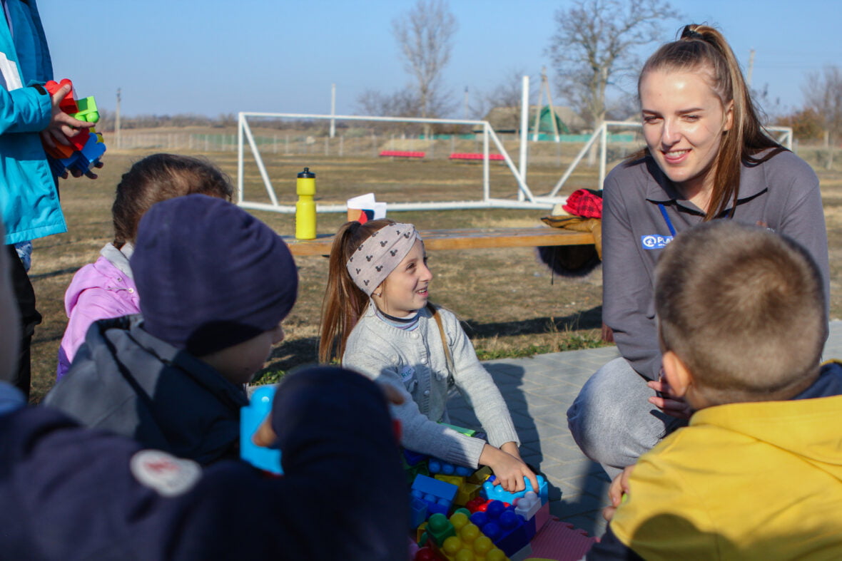 Planin työntekijä juttelee lapsille urheilukentällä Moldovassa.