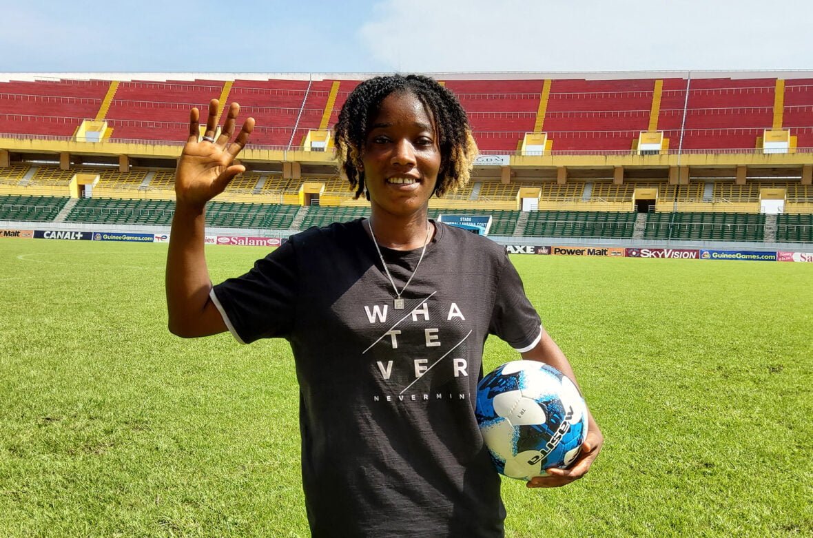 Guinealainen Tombody poseeraa jalkapallon kanssa stadionilla.