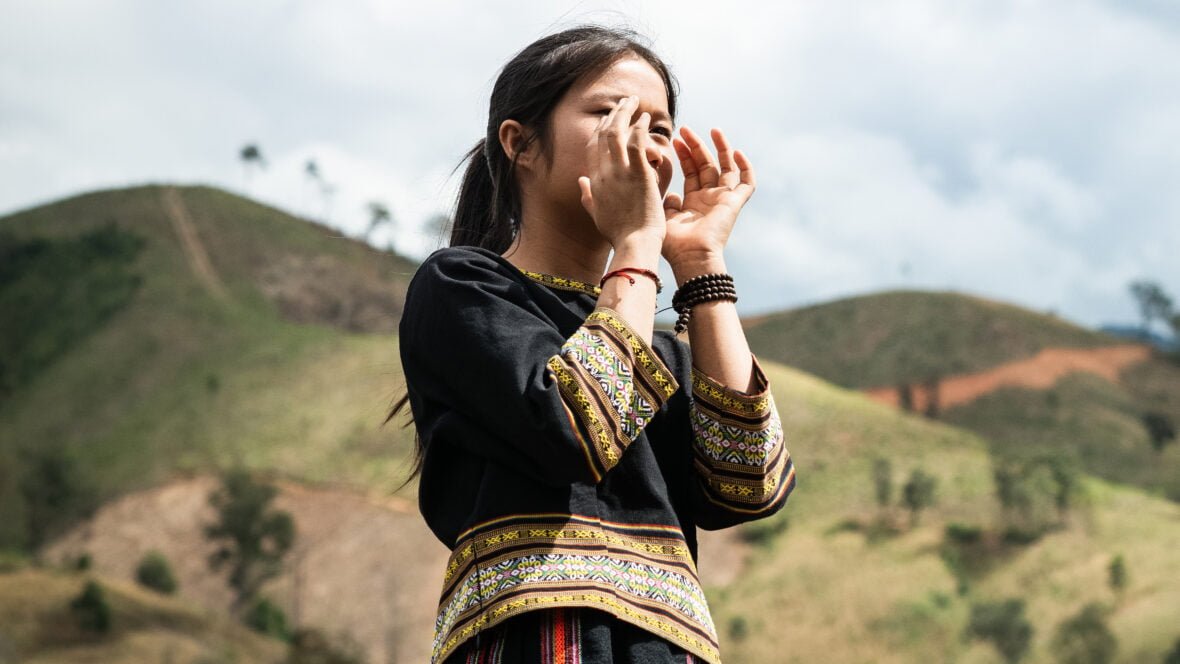 Tyttö huutaa kädet suun ympärille laitettuna vuoristomaisemassa Vietnamissa.
