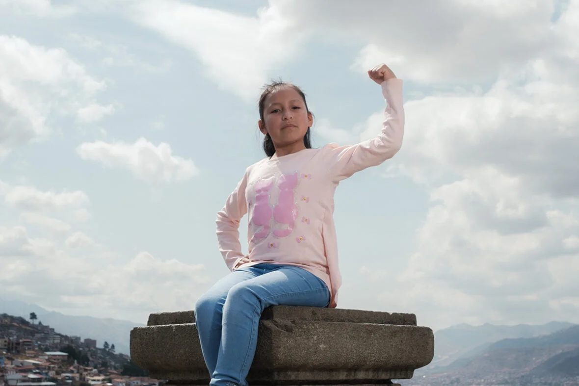 10-vuotias Briyit istuu kuvassa kivisen pylvään päällä, vasen kätensä koukistettuna nyrkki kohti taivasta. Tytöllä on kasvoillaan päättäväinen ilme ja hän katsoo suoraan kameraan.