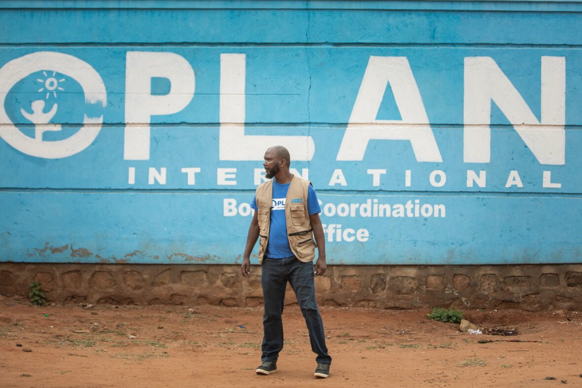 Planin työntekijä Etiopiassa ison seinän edessä, johon on maalattu Planin logo.