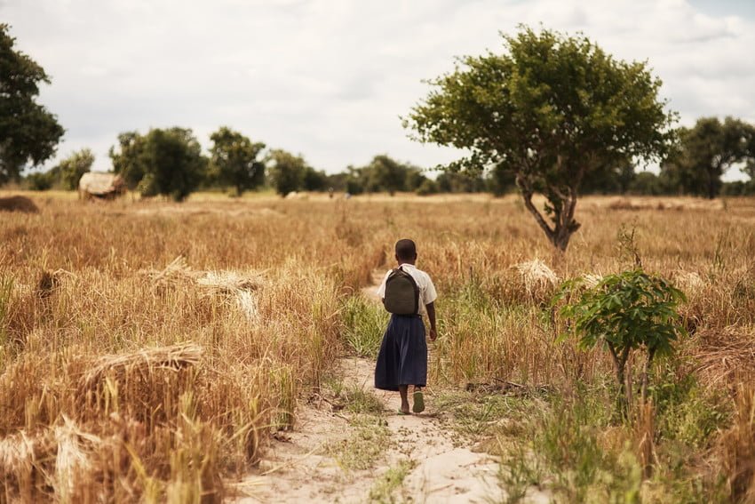 Lapsi kävelee savannimaisemassa poispäin kuvaajasta.