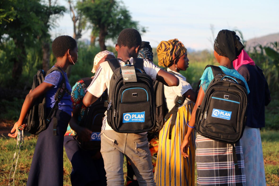 Lapsia Mosambikissa seisomassa ulkona koulureput selässä. Planin työ Mosambikissa ja Myanmarissa jatkuu.
