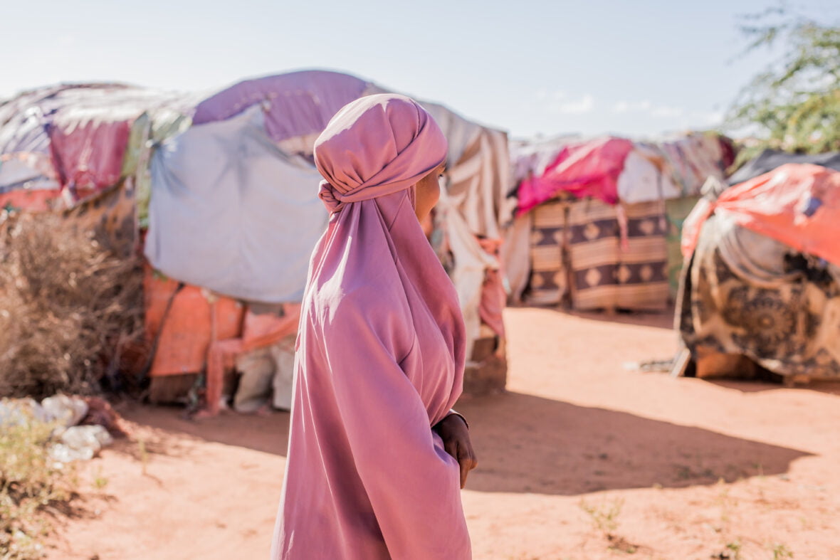 Tyttö seisoo poispäin kamerasta pakolaisleirin rakennusten keskellä Somaliassa.