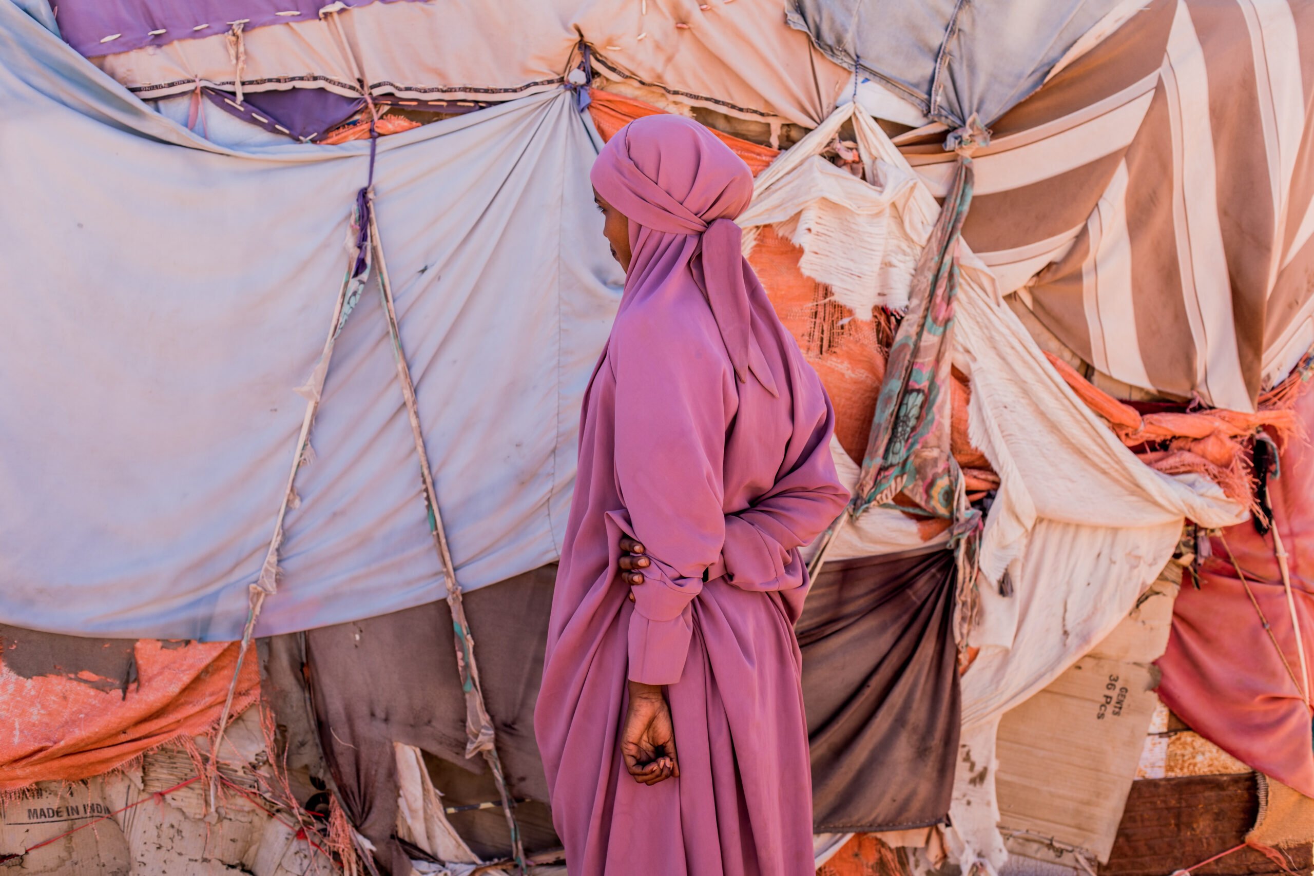 Tyttö seisoo poispäin kamerasta pakolaisleirin rakennusten keskellä Somaliassa.