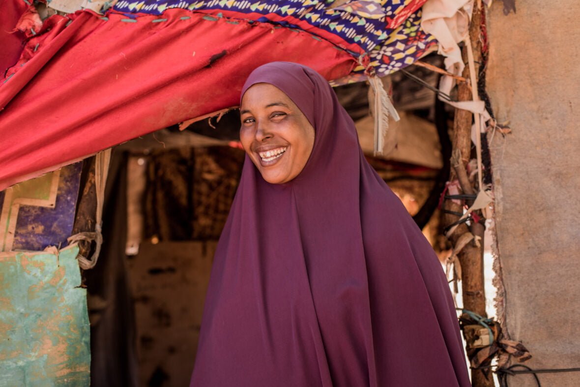 Nainen nauraa iloisena kameralle kotinsa edustalla pakolaisleirillä Somaliassa.