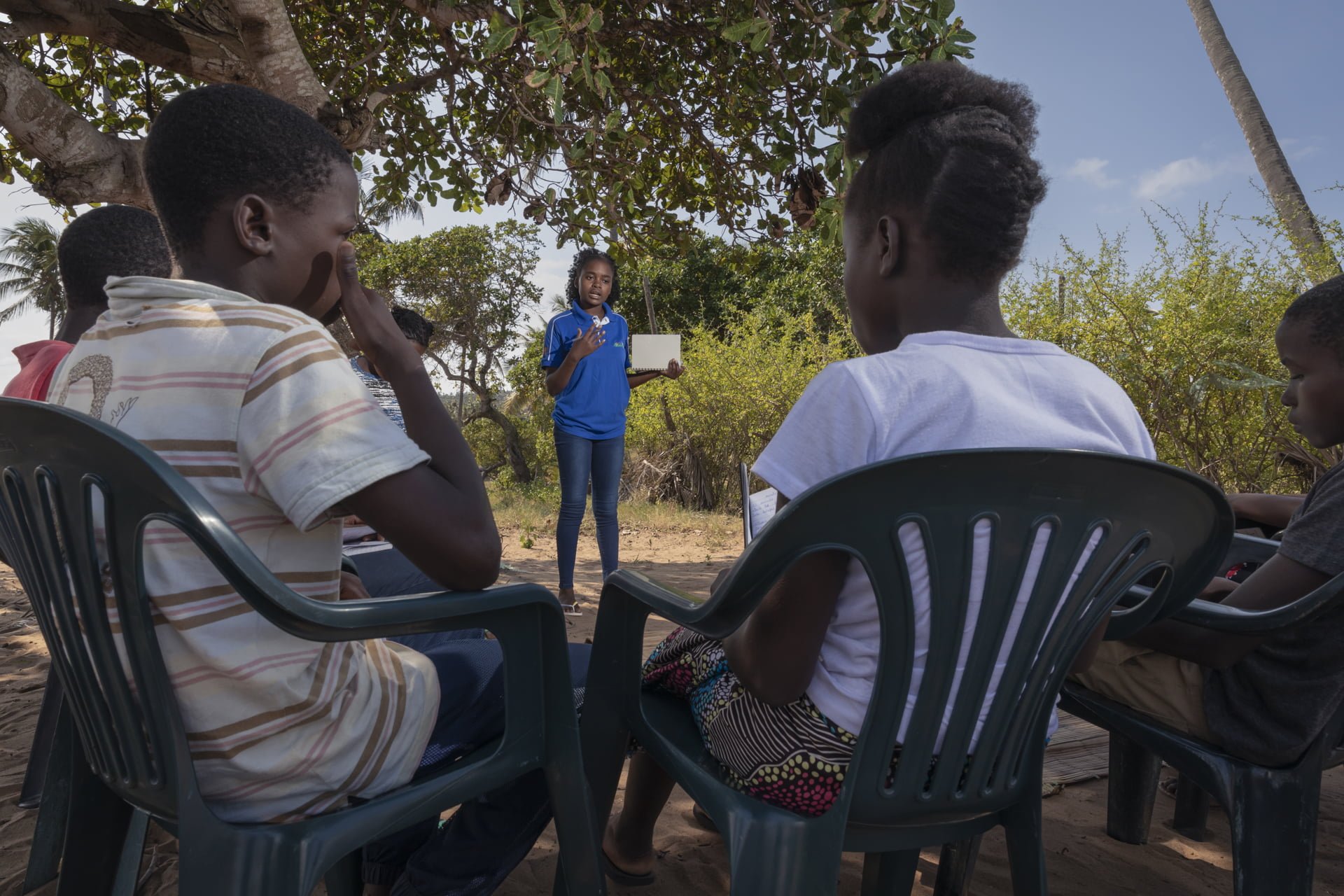 Mosambikilainen Eunice seisoo ja puhuu ihmisille, jotka kuuntelevat tuoleissa istuen.