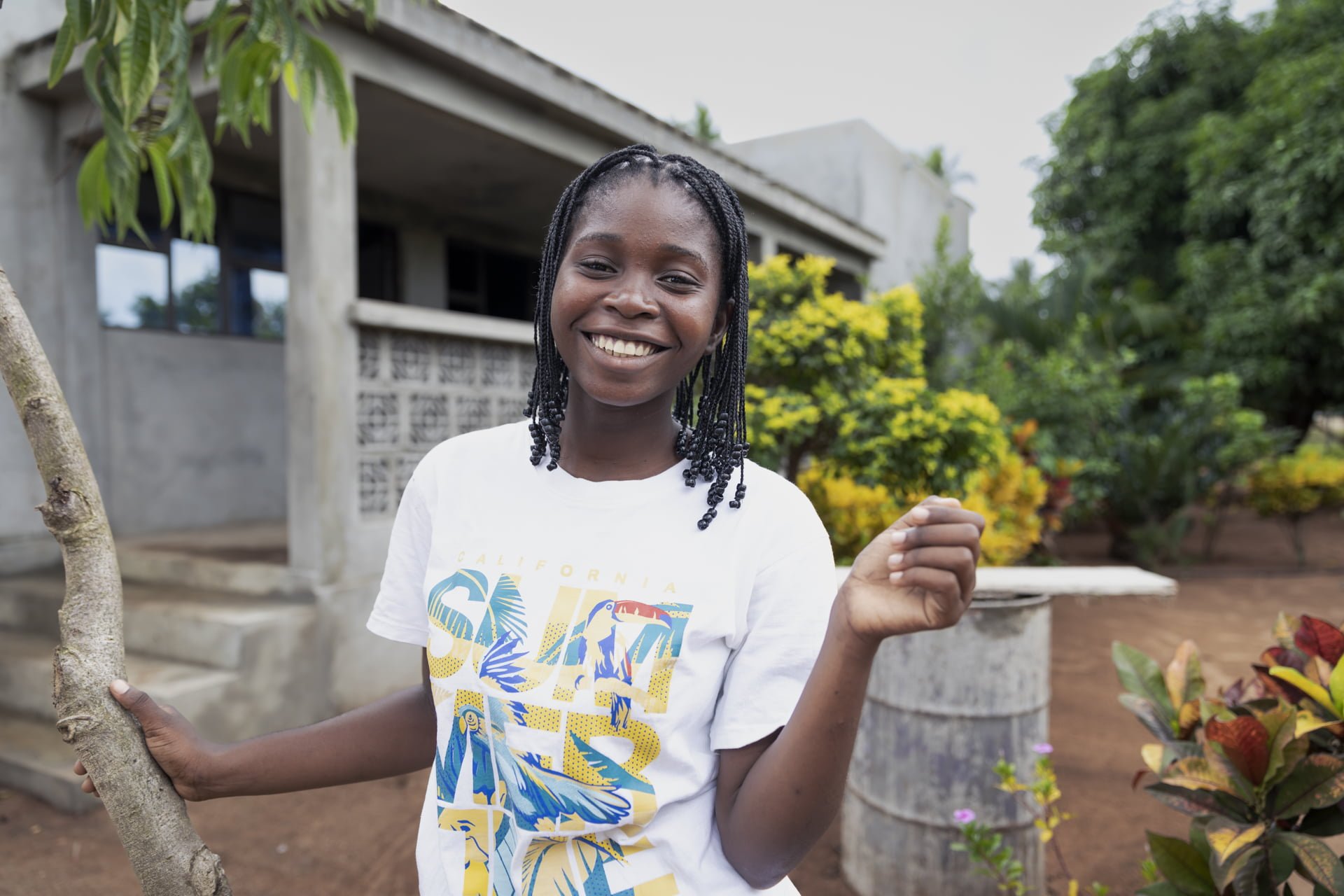Mosambikilainen Denise hymyilee iloisena rakennuksen pihalla.