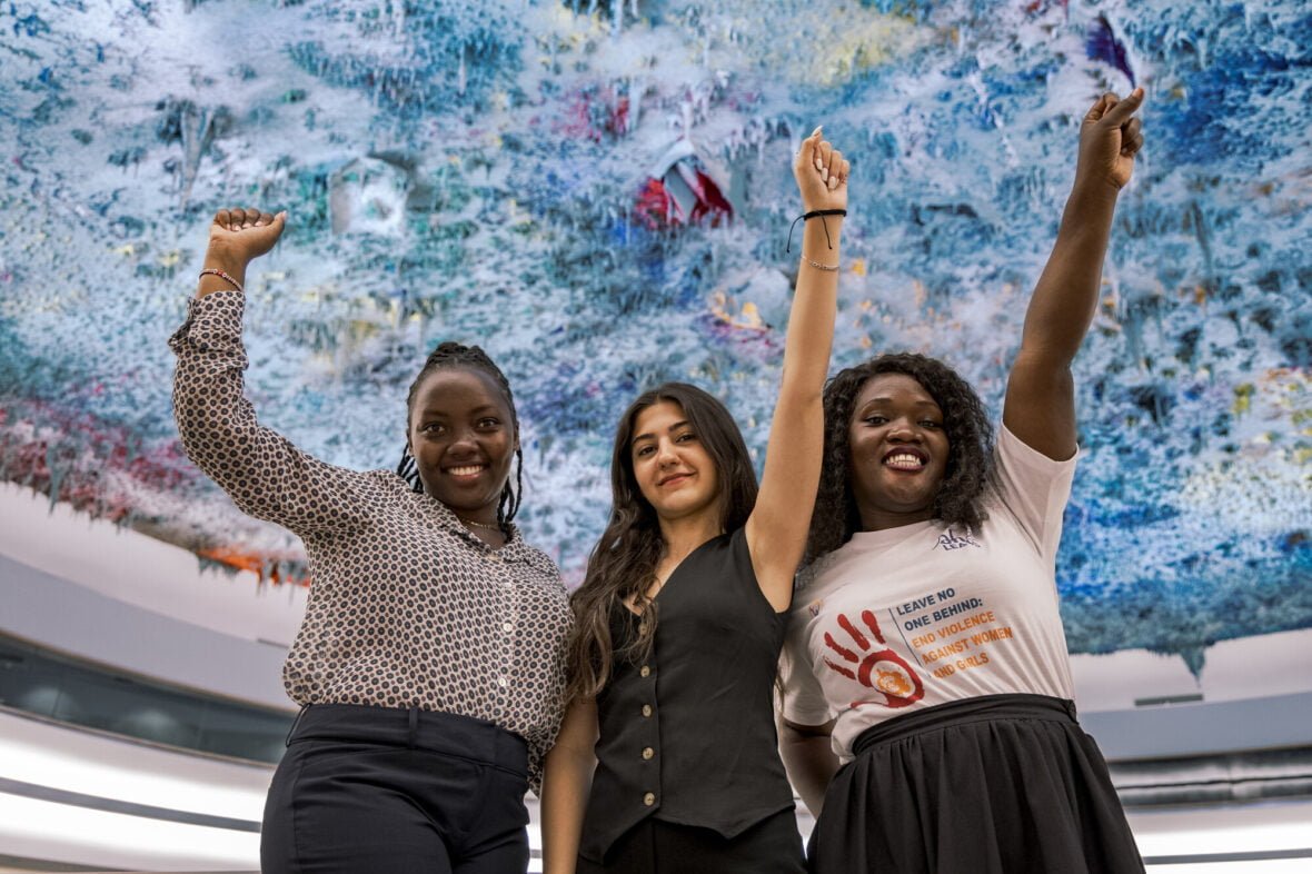 Racheal ja kaksi muuta nuorta aktivistia seisoo YK:n tiloissa Genevessä kädet ilmassa.