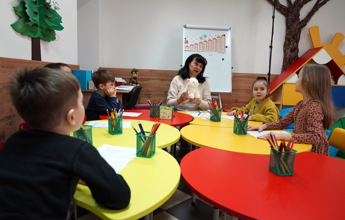 Ukrainalaiset lapset istuvat pöydän ympärillä lapsiystävällisessä tilassa.