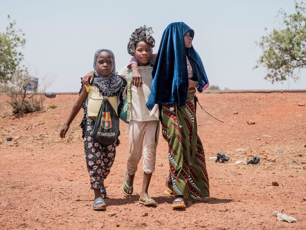 Kolme tyttöä kävelee kuivuuden koettelamassa ympäristössä kädet toistensa harteilla.