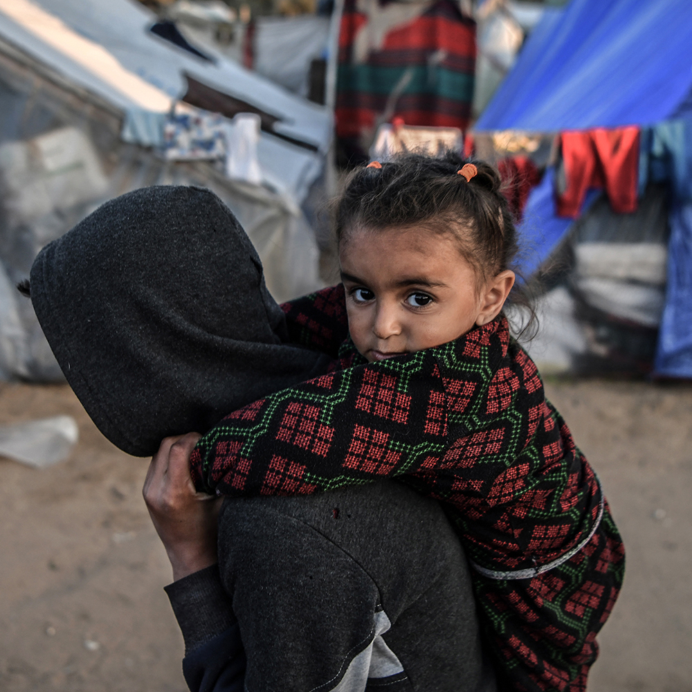 Tyttö Gazassa pakolaisleirillä pojan reppuselässä katsoo kameraan.