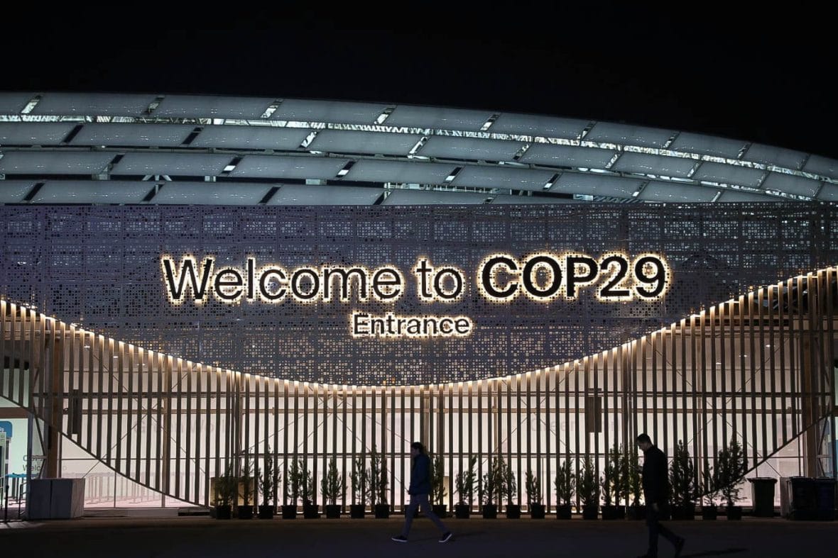 Konferenssirakennus, jonka seinässä lukee "Welcome to COP29", etualalla ihmisiä silhuetteina.