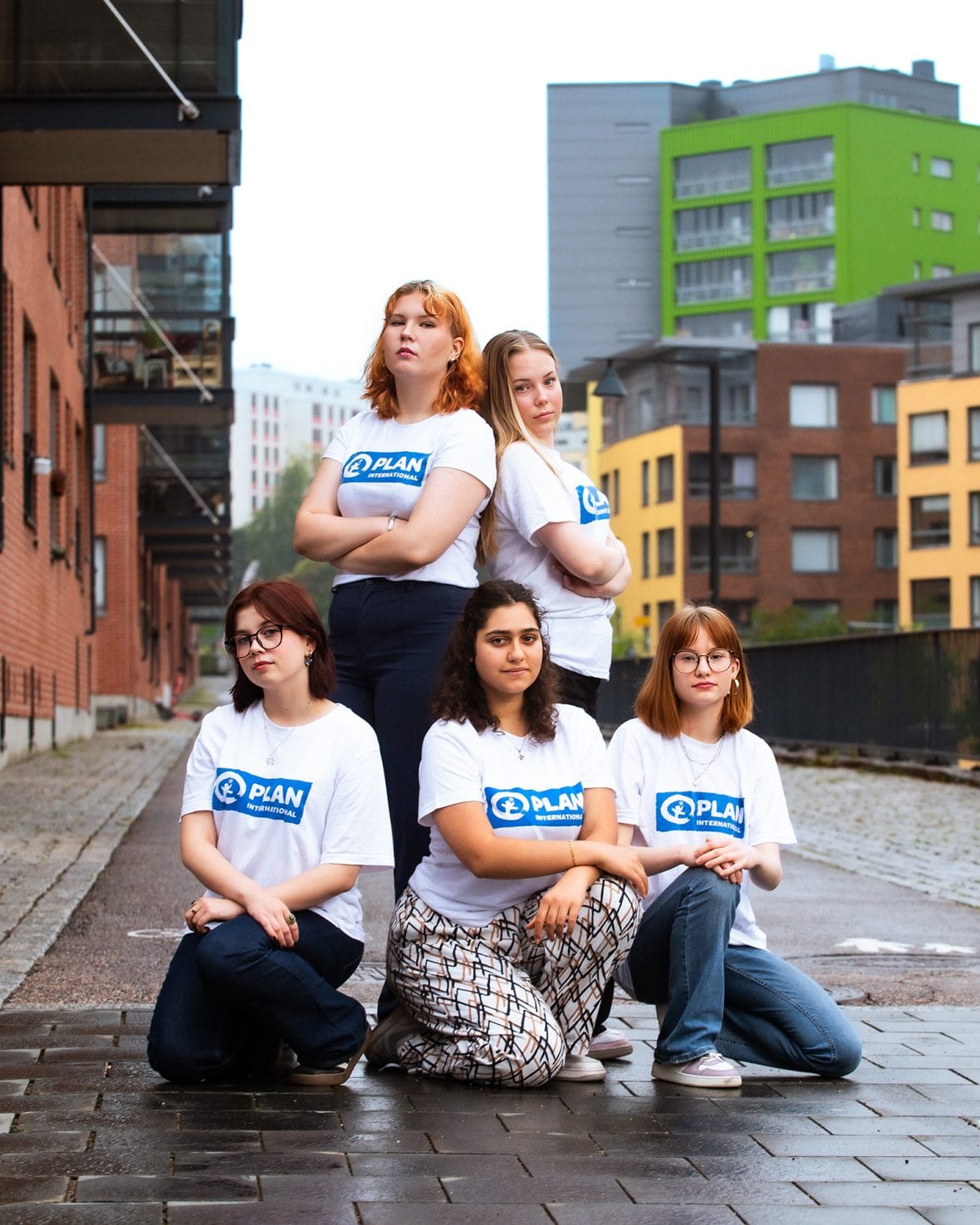 Viisi GirlsTakeover-nuorta ryhmäkuvassa, kaupunkimaisemaa taustalla.