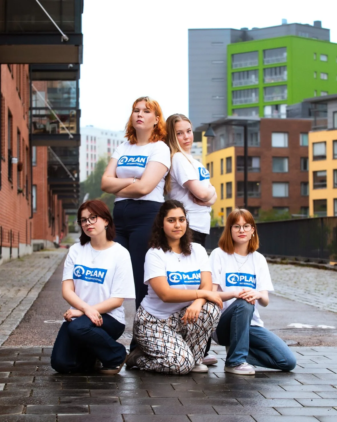 Viisi GirlsTakeover-nuorta ryhmäkuvassa, kaupunkimaisemaa taustalla.