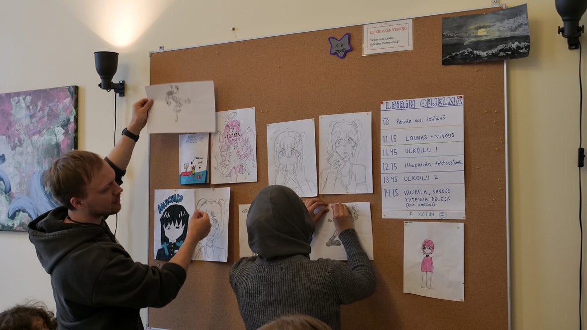 Kaksi nuorta kiinnittää piirroksia seinälle.