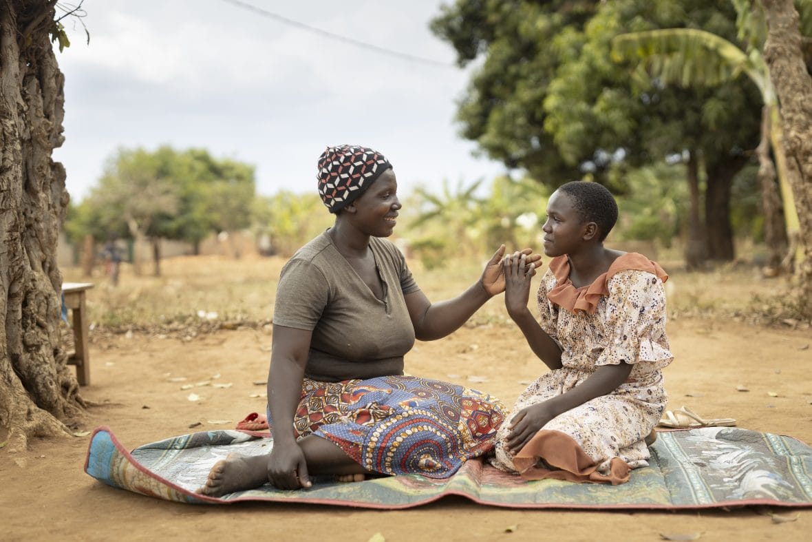 Kaksi naista istuu matolla ja hymyilee toisilleen Ugandassa