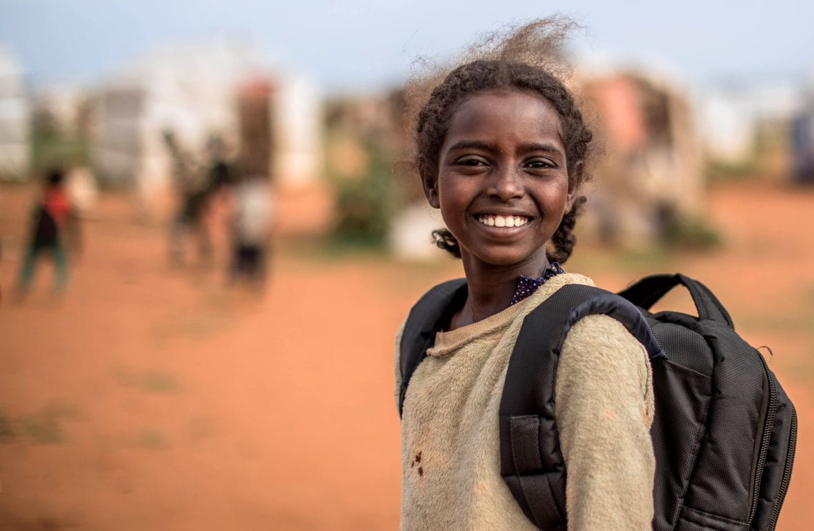 Tyttö hymyilee koulureppu selässä.