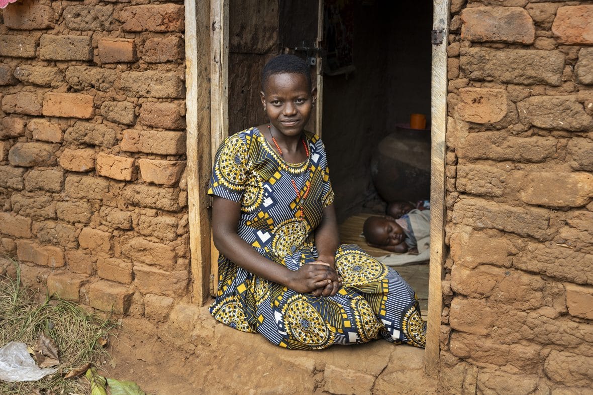 Ugandalainen Catherine istuu talonsa ovella, ovesta näkyy sisällä nukkuvaa kaksi lasta.